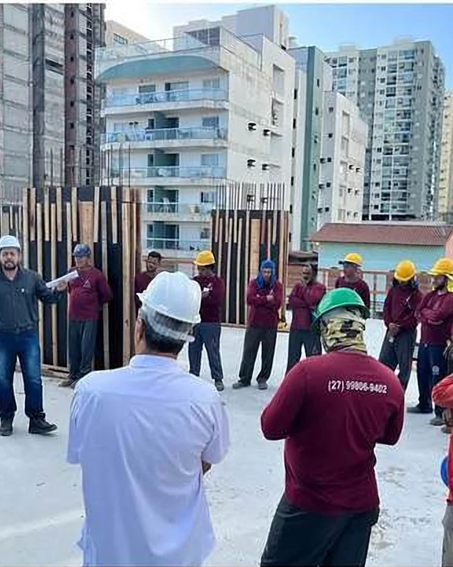 Willyam Souza conduzindo um diálogo de segurança com operários de capacete em um canteiro de obras