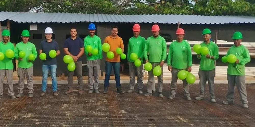 Equipe com uniformes verdes, capacetes e EPIs em frente a uma obra